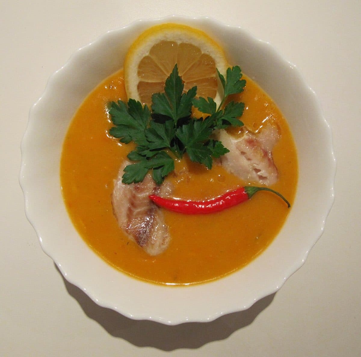 Pomarańczowa zupa rybna z kawałkami ryby, plasterkiem cytryny, chili i natką
